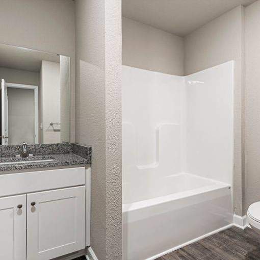 Three-Bedroom Townhomes in Belton, MO - Traditions Townhomes - Bathroom with Vinyl Plank Flooring, Built-in Bathtub, Single Vanity, Sink, Mirror, and White Cabinetry.