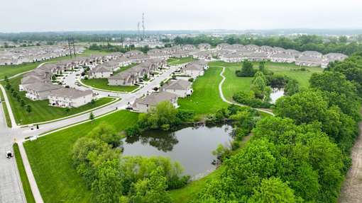 A bird's eye view of a residential area with houses, a pond, and a road.