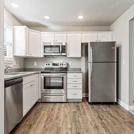 Townhomes for Rent in Belton, MO - Traditions Townhomes - Kitchen with Vinyl Plank Flooring, High Ceiling, Granite Countertop, White Cabinetry, and Stainless Steel Appliances.