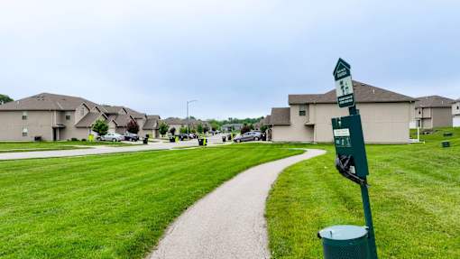 A green signpost stands in a grassy area with a path leading to a residential area.