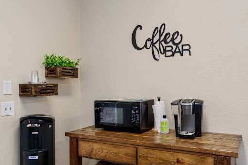 A coffee bar with a coffee maker, microwave, and a coffee pot on a wooden table.