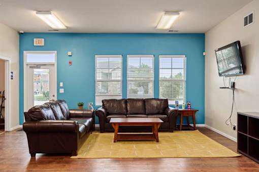 Lawrence, KS, Apartments Near University of Kansas - Remington Square - Resident Lounge with Wood Flooring, Two Brown Leather Couches, Coffee Table, Side Tables, Mounted TV, and Light Fixtures.