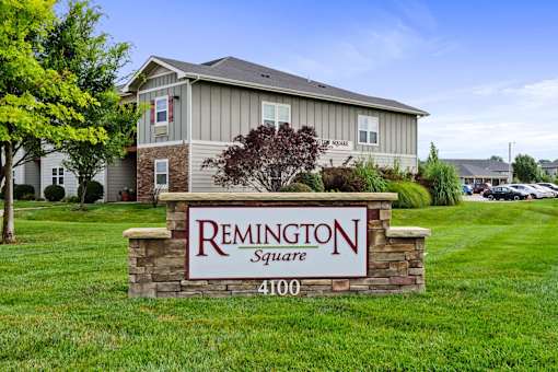 A sign for Remington Square with a house in the background.