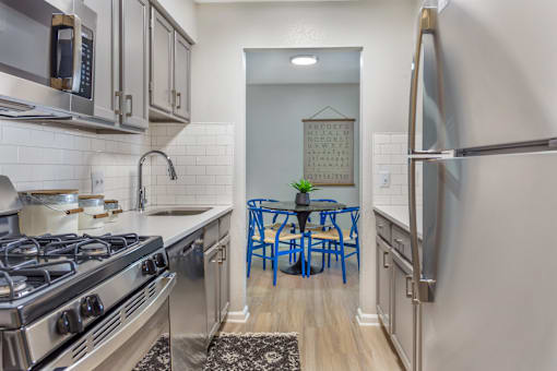 A kitchen with a stove, refrigerator, and blue chairs.