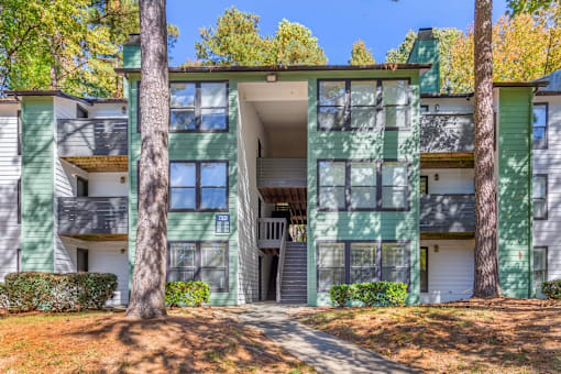 A green and white apartment building with a tree in front.