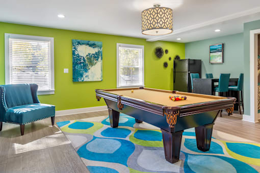 A pool table is in the middle of a room with a blue chair and a green wall.