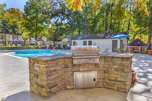 A stone wall with a grill on top and a pool in the background.