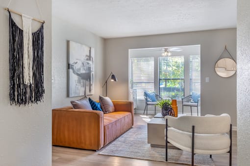 A living room with a brown couch, a white chair, and a hanging decoration on the wall.