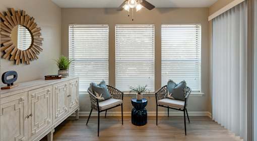 A living room with a wooden floor, a white cabinet, a mirror, a ceiling fan, and a window with blinds.