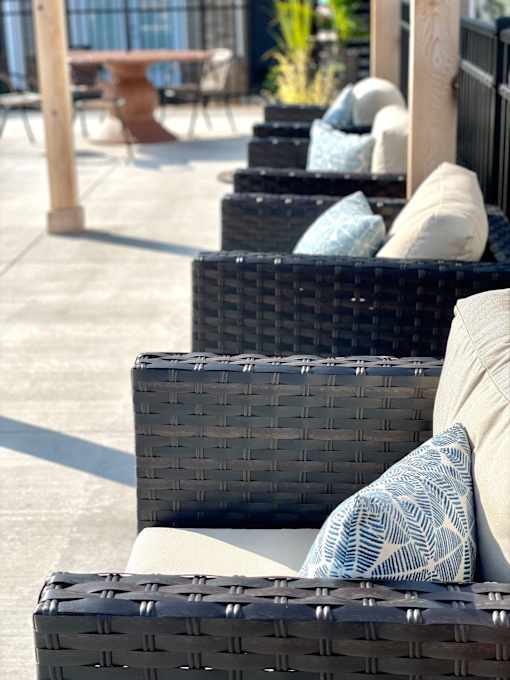 A row of black wicker chairs with cushions are lined up on a patio.