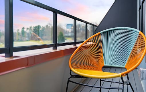 A chair with a yellow seat and green back is placed on a balcony.