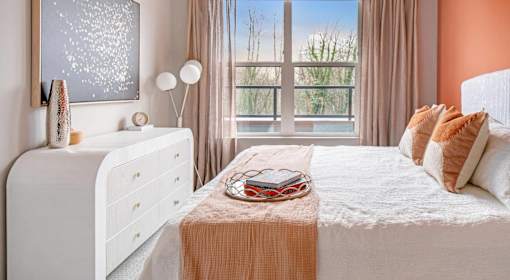 A bedroom with a white bed, a white dresser, and a window with a view of trees.