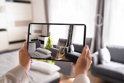 A person is holding a tablet with a photo of a living room on the screen.