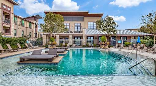 A large swimming pool in front of a building with lounge chairs around it.