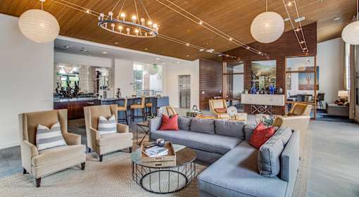 A living room with a grey couch and wooden chairs.