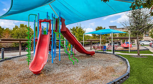 A playground with a red slide and a blue canopy.