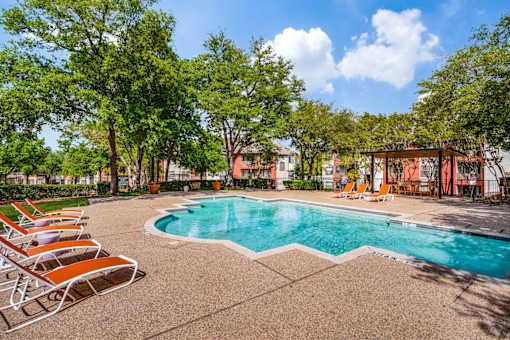 A pool surrounded by trees and chairs.
