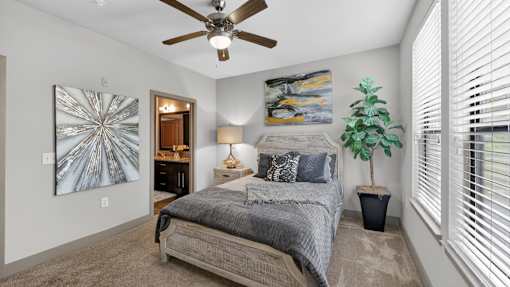 A bedroom with a bed, a ceiling fan, and a potted plant.