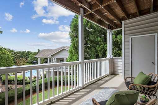 A porch with a white railing and a green pillow.