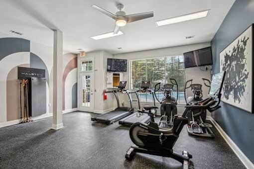 A gym with a row of treadmilers and a fan.