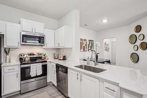 A white kitchen with a stove, oven, microwave, and sink.