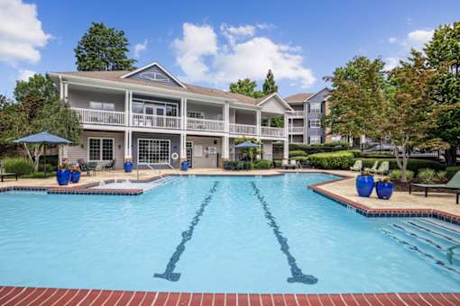 A large swimming pool in front of a building with a blue umbrella and two blue chairs.