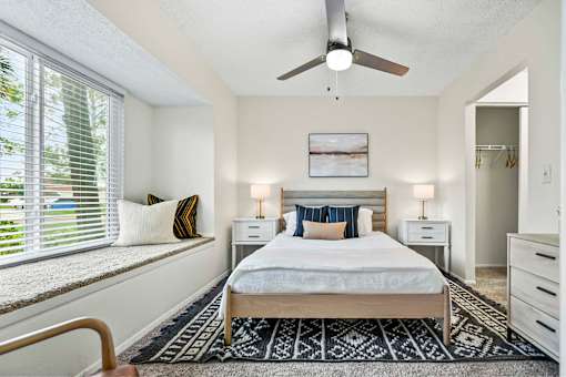 A bedroom with a bed, two nightstands, a ceiling fan, and a window with blinds.