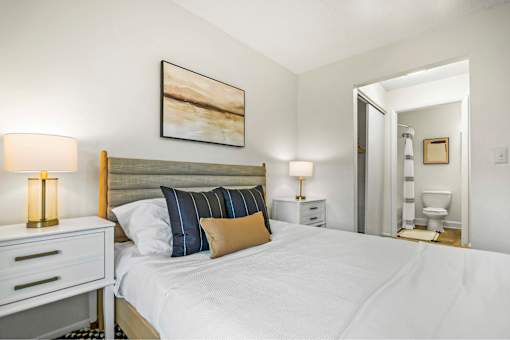 A bedroom with a large bed, two nightstands with lamps, and a painting on the wall.