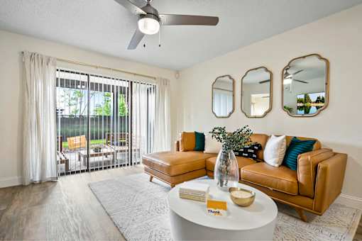 A living room with a tan couch, a white coffee table, and a ceiling fan.