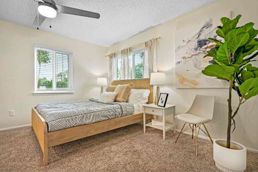 A bedroom with a bed, desk, chair, and a plant.