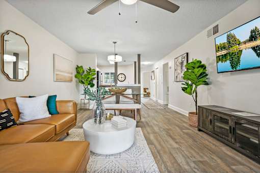 A living room with a brown leather couch, a white coffee table, and a flat screen TV mounted on the wall.