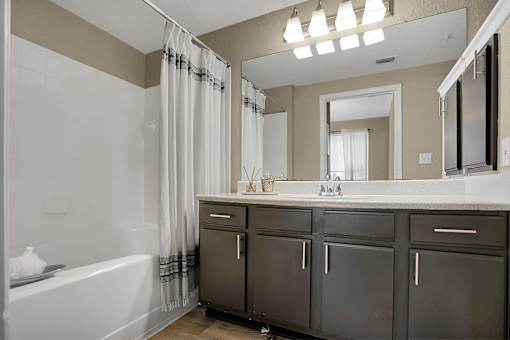 A bathroom with a white tub, sink, and grey cabinets.