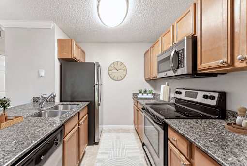 A kitchen with a black refrigerator and stove, wooden cabinets, and a clock on the wall.