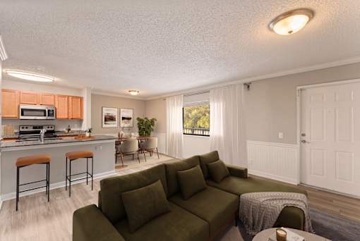 A living room with a green couch and a kitchen area with orange cabinets.