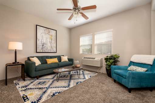 A living room with a green couch, a blue couch, a rug, and a ceiling fan.