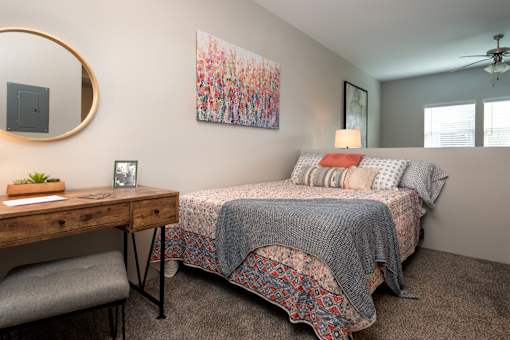 A bedroom with a bed, desk, chair, and a painting on the wall.