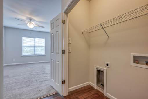 A room with a white door, a window with blinds, a ceiling fan, and a shelf with some items.