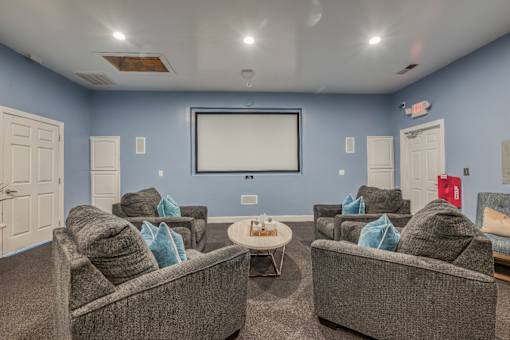 A living room with grey couches and a white screen.