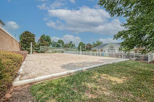 A large, empty sand pit sits in the middle of a grassy area.