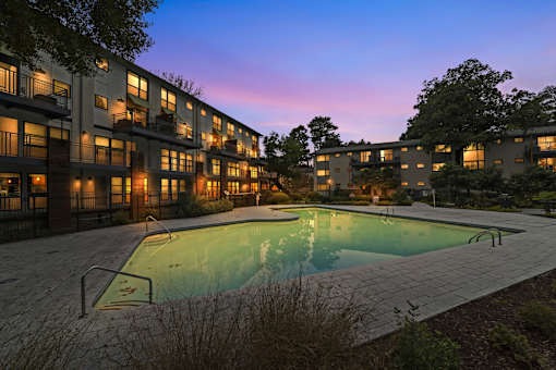 A swimming pool is surrounded by apartment buildings at dusk.