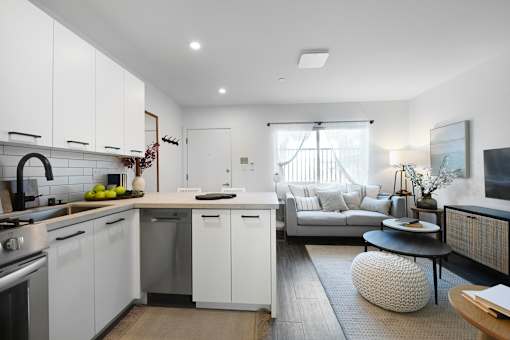 A modern kitchen with white cabinets and a grey sofa.
