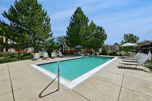 A swimming pool surrounded by trees and chairs.