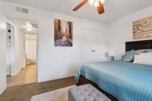A bedroom with a bed, a ceiling fan, and a painting on the wall.