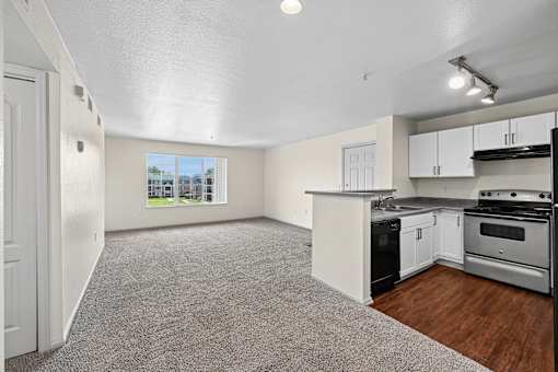 A spacious living area with a kitchen and a view of a parking lot through the window.