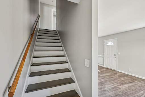 A staircase with wooden handrails and grey steps leads to a white door.