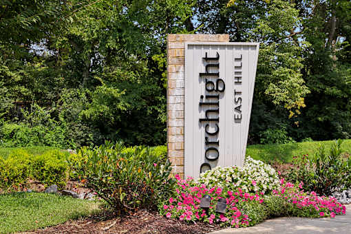 A sign for Porchlight East Hill surrounded by flowers.