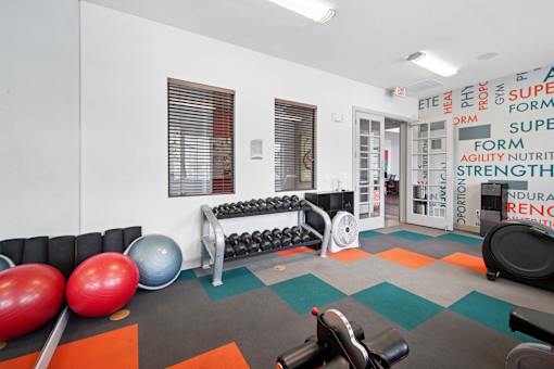 A gym with a variety of equipment including dumbbells, exercise balls, and a bench press.