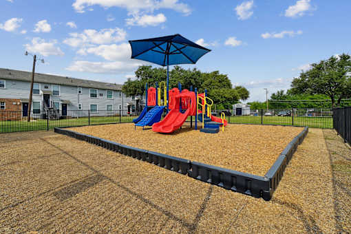 A playground with a slide, swings, and a blue umbrella.