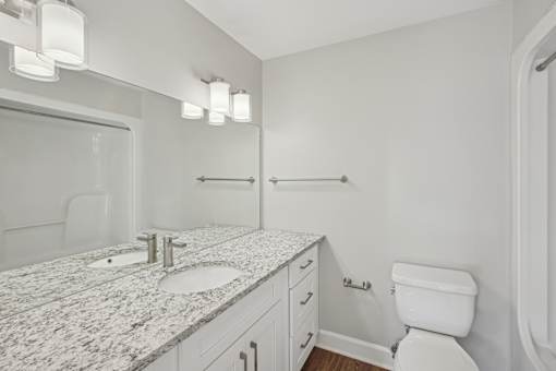 A white bathroom with a marble counter top and a toilet.