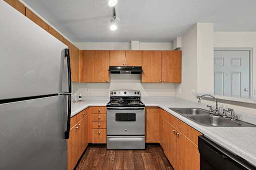 A kitchen with a stainless steel refrigerator, a stove, and wooden cabinets.